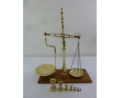 An early 20th century brass balance scale on raised wooden plinth, to include seven weights