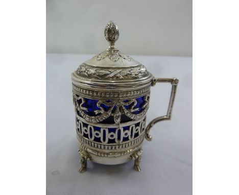 Russian white metal mustard pot, scroll pierced sides, the hinged embossed cover with bud finial all on four paw feet to incl