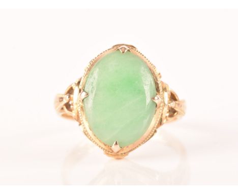 A yellow metal dress ring, set with a cabochon oval jade measuring approximately 14mm length x 10.5mm width, in a ornate sett