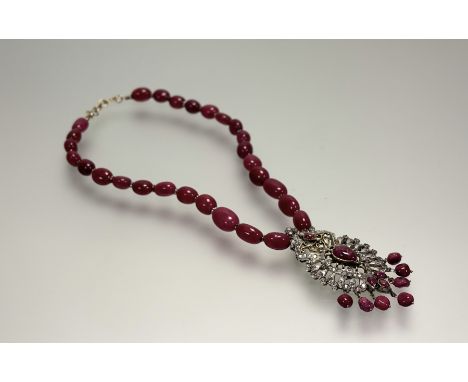 An eastern yellow and white metal pendant necklace with ruby beads and metal spacer suspending a paste and ruby set open work