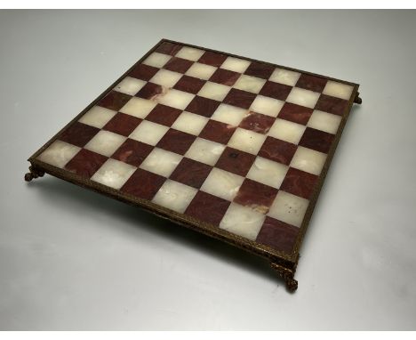 A marble and onyx chess board, with elaborately decorated brass edges and raised on four claw feet (h. 4cm, 41cm x 41cm) 