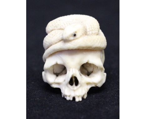 A Japanese ivory netsuke, Meiji period, modelled as a skull with a serpent curled on the top, 3cm.Condition: negligible signs