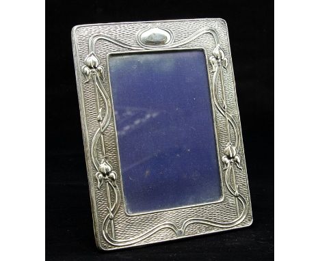 An Edwardian Art Nouveau silver photo frame, with sinuous decoration and tulip motifs on an engine turned ground, velvet ease