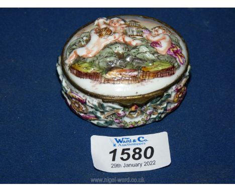 A ceramic trinket box with cherub and flower design, 2 /3/4" diameter x 1 1/2" tall.