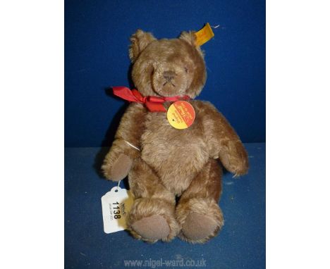 A light brown Steiff jointed Teddy Bear 'Knopf Im OHR', no. 0202/26, with button tag and red bow, 9 3/4'' tall