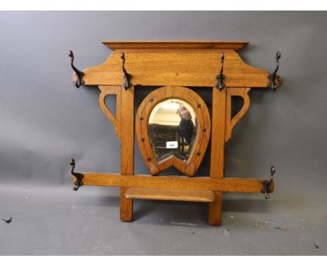 An Arts & Crafts golden oak hanging coat rack with a horseshoe framed bevelled glass mirror 