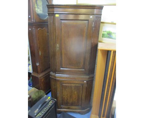 An early 19th century oak corner cabinet, the top with door flanked by fluted carved decoration, and painted interior shelves