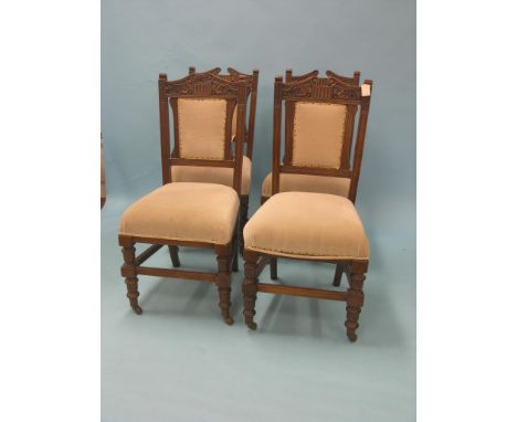 A set of four late Victorian walnut dining chairs, carved, architectural crestings above upholstered seats and backs, on cast