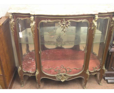 A large Louis XV-style mahogany display cabinet, serpentine-shape with elaborate ormolu mounts and variegated marble top, sin