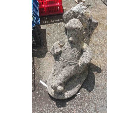 A vintage concrete garden ornament in the form of a gnome seated in an armchair