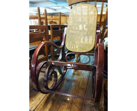 A vintage style stained wood framed rocking chair with rattan back and seat panels, set on bentwood scroll supports