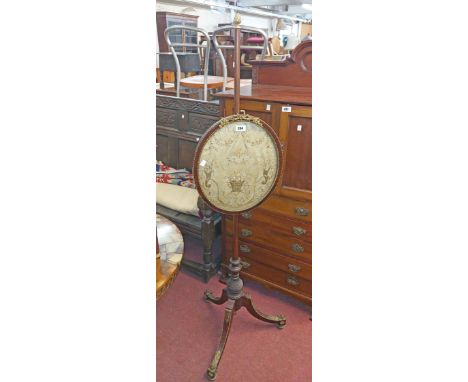 An early 19th Century gilt metal mounted mahogany pole screen with oval silk embroidery panel under glass, set on a slender t