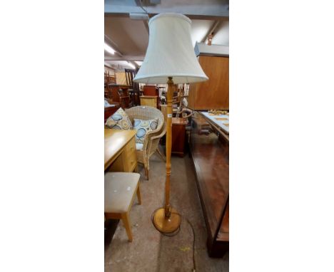 A polished pine standard lamp with slender turned pillar, circular base and shade