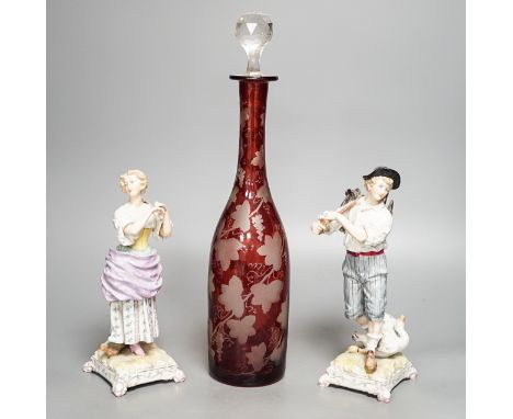 A late 19th century Bohemian wheel engraved ruby glass decanter and a pair of continental porcelain figures, decanter 37 cms 