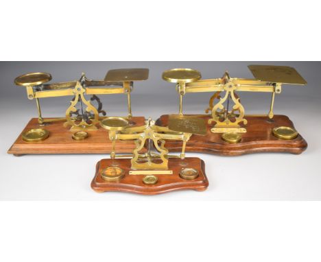 Three sets of brass postage scales, two with rates to pans, the other with ivorine plaque to base, length of longest 31cm