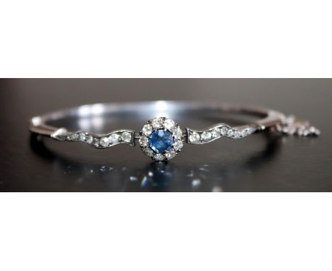 Edwardian White Gold Diamond And Sapphire Hinged Bangle, Central Sapphire Surrounded By Nine Round Cut Diamonds Between Two R