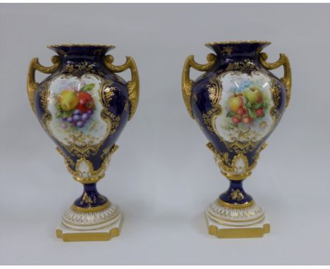 A pair of Royal Worcester vases with gilt twin handles and hand painted fruit panels, signed Hawkins, to a blue ground, with 