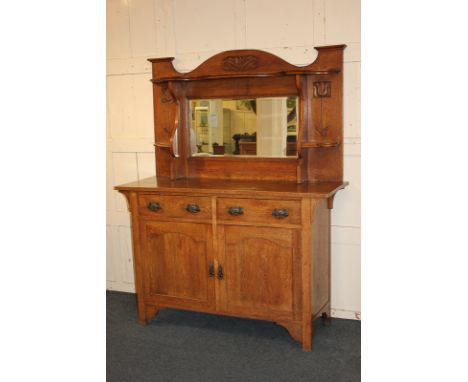 An Arts &amp; Crafts Liberty style oak sideboard, raised back with shelf and mirror carved with stylised flowers, above base 