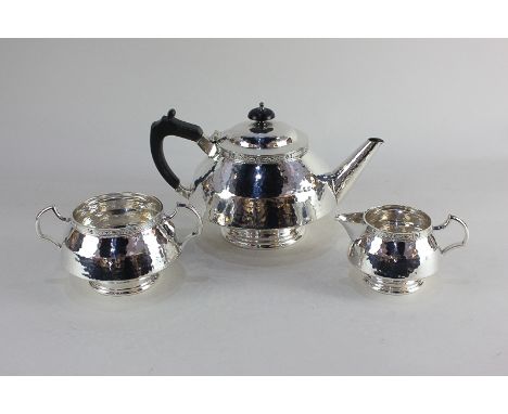 An Arts and Crafts style silver plated three-piece tea set of teapot, sugar bowl and milk jug, circular form with textured be