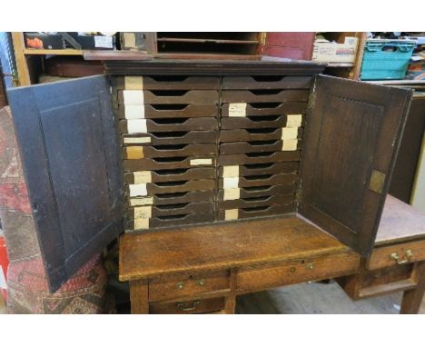 An early 20th century office stationery cabinet, fitted with two blind panel doors, opening to reveal 24 slide out trays, wid