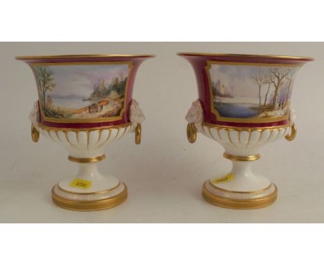 A pair of modern Royal Worcester urns, decorated with landscape panels to a burgundy ground by Frank Clark, having lion's mas