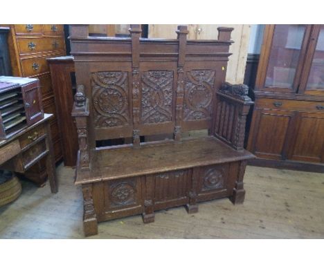 An oak box seat settle, having thee panels to the back, carved with shields, fruiting vine and scrolls, with Gothic style sid