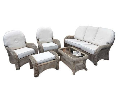 A rattan five piece conservatory suite, comprising a three-seater sofa, two elbow chairs, a footstool and a glass topped coff