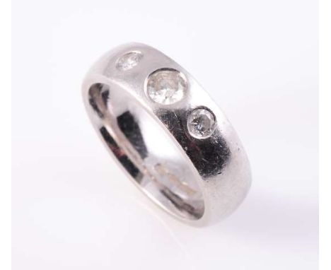 A DIAMOND RING, the three graduating brilliant cut diamonds channel set in separate settings in a simple heavy band. Stamped 