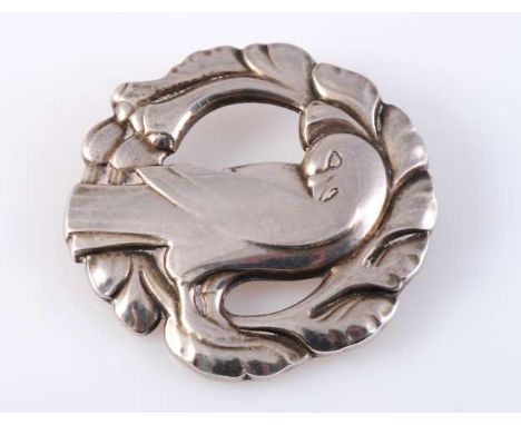 A GEORG JENSEN SILVER BROOCH, the circular brooch of moulded metal work depicting a dove amongst foliage, set simply on a bro