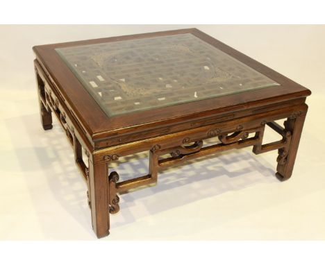 A CHINESE HARDWOOD COFFEE TABLE, the square top with glass inset above a fret carved panel, raised on moulded square-section 
