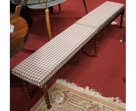 An extremely long oak luggage seat, having typical slatted top raised on bobbin supports, with twin removable chequer cushion