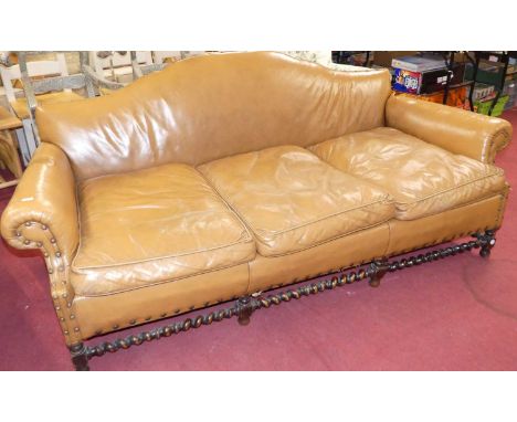 An early 20th century oak framed and tan leather upholstered and further studded three seater sofa, having a gentle hump back