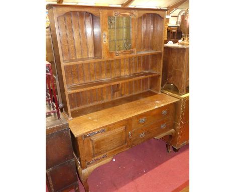 An early 20th century oak and copper mounted kitchen dresser, having lead glazed central upper door, open plate racks over ba