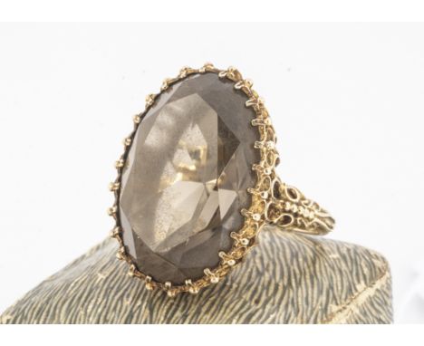 A 9ct smoky quartz dress ring, of oval mixed cut, in a claw setting on a raised oval basket, ornate shoulders, ring size k, 1