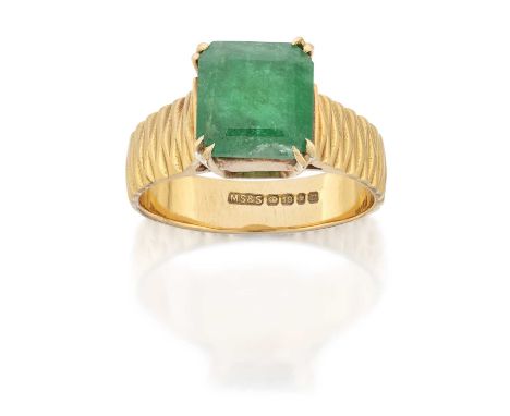 An 18 Carat Gold Emerald Ring, the emerald-cut emerald in a yellow double claw setting, to a broad textured shank, finger siz