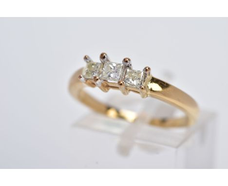 A YELLOW METAL THREE STONE DIAMOND RING, designed with a raised row of three claw set princess cut diamonds, total estimated 