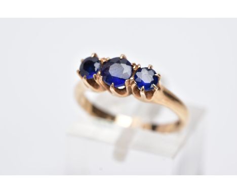 A YELLOW METAL THREE STONE RING, designed with three graduated circular cut blue stones assessed as a blue glass doublets, to