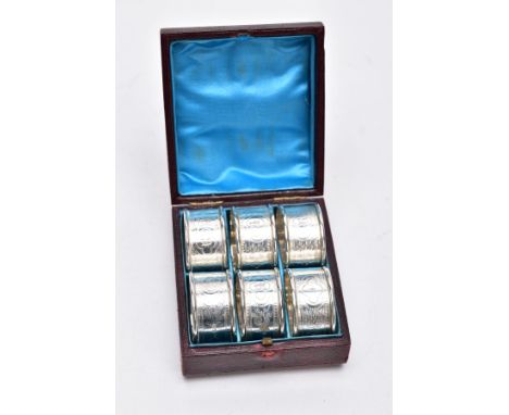 A CASED SET OF SIX SILVER NAPKIN RINGS, each with a decorative foliate and scroll detail with an engraved 'R' and numbers fro