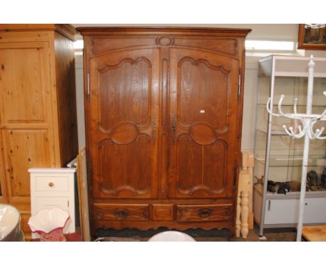 A large oak French armoire, with interior shelf and hanging compartment, two long drawers below, raised on squat cabriole sup