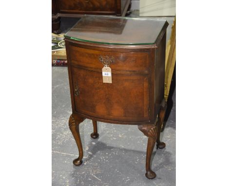 A mid 20th Century bow front walnut bedside cupboard The cross banded top above single cupboard door, raised upon shelf carve