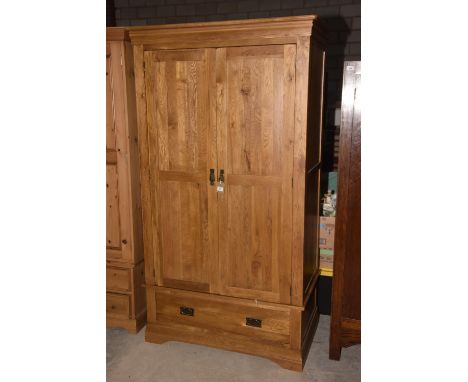 A contemporary light oak wardrobeHaving a moulded cornice above two panelled doors and a single drawer, raised upon  a plinth