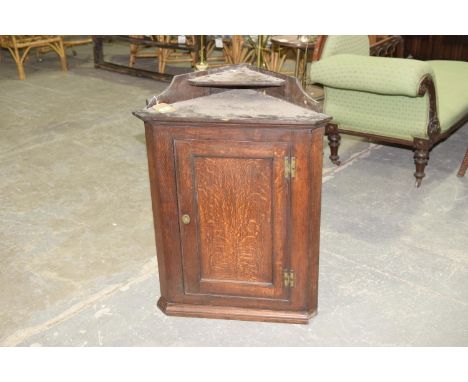 An 18th Century oak hanging corner cupboardHaving an upper shelf above a single panelled door enclosing two shaped fixed shel