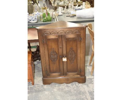 A reproduction oak freestanding corner cupboardHaving a pair of carved cupboard doors above a shaped apron with bracket feet,