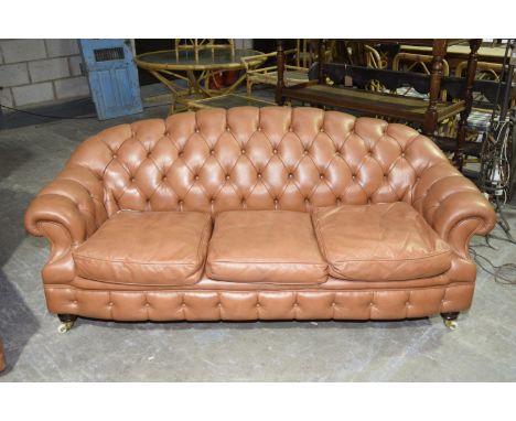 A tan leatherette Chesterfield type setteeHaving an arched padded button back above three loose cushions enclosed by padded s