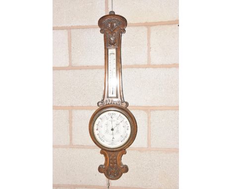 A Victorian carved oak Banjo wall barometerThe carved frame applied with a enameled dial and thermometer above a 20cm enamele