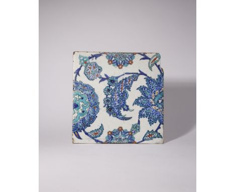 AN IZNIK SQUARE TILE 17TH CENTURY Painted in blue, red and turquoise with saz leaves and stylised blooms, the design set on a