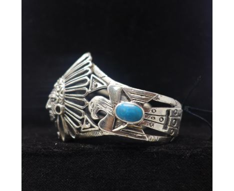 A sterling silver large bangle in the form of an American Indian with turquoise cabochon panels, Dia: 7cm, 51.5g 