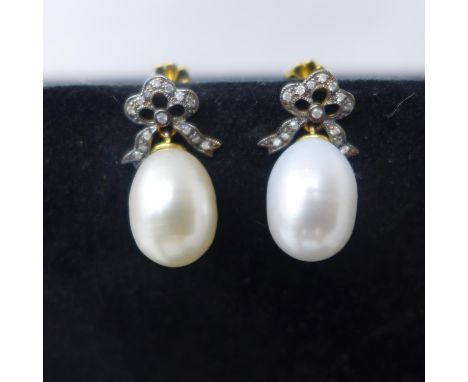A boxed pair of yellow gold set to ther top with diamond-studded bows and suspended by a large, cream-coloured cultured pearl