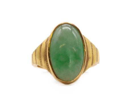 A gold single stone jade ring, with an oval jade cabochon, rub set, to tapering engraved shoulders and a flat section shank, 