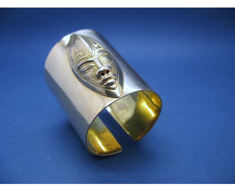 An Unusual Cuff Bangle, of plain tapering form, detailed to the front with an elongated tribal mask, indistinctly stamped and